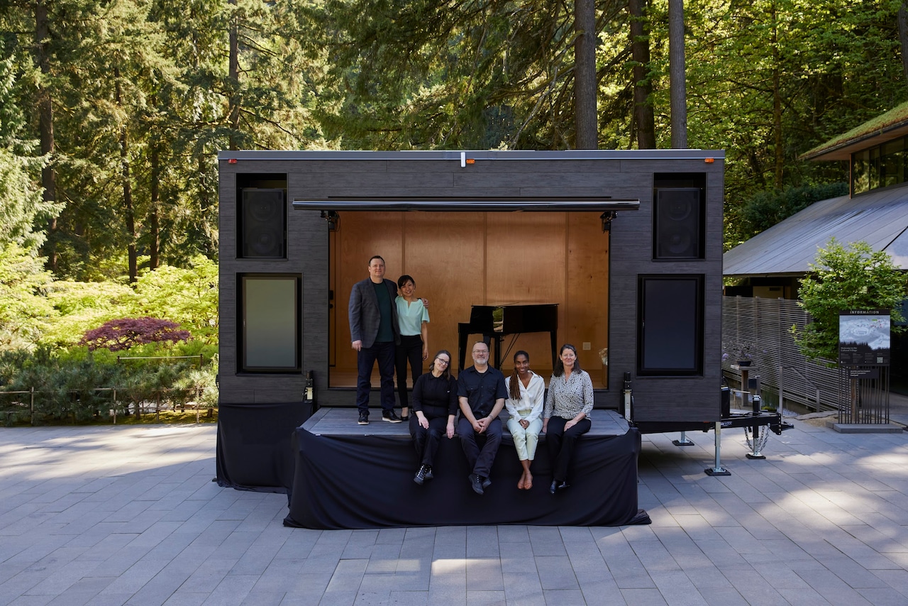 Curators and performers in the Summer Series pose in front of SoundsTruck NW's mobile venue, a trailer with a stage and awning that extend to display a piano and space for performances.