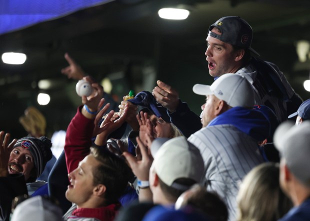 Fans in the bleachers reach for a tossed ball from...