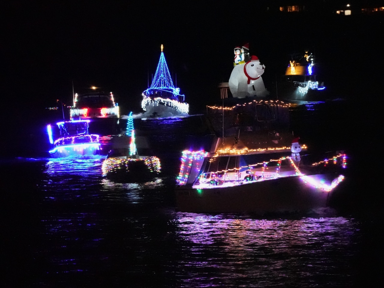 seven ships in a row decorated in Christmas lights on a river at night