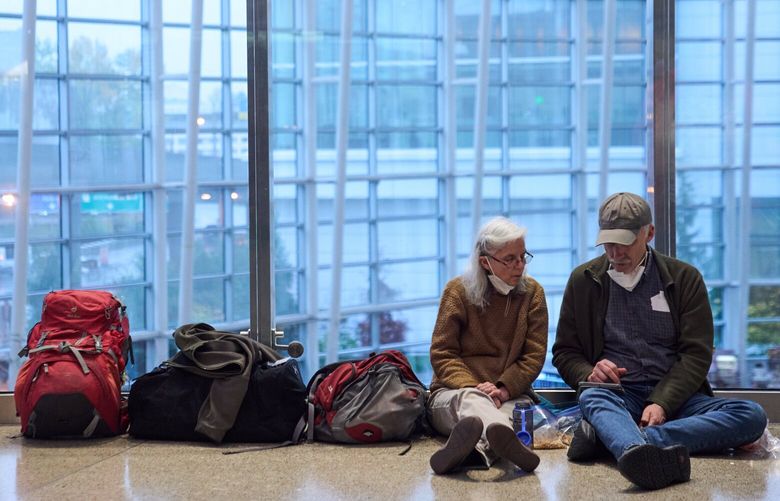 Travelers sit with their luggage at Seattle-Tacoma International Airport Thursday, Nov. 6, 2025, in SeaTac, Wash.