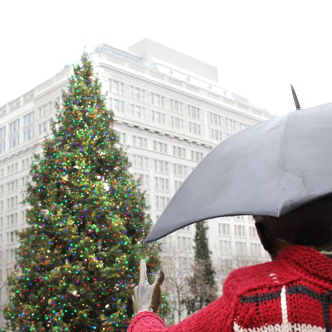 a large tree decorated with lights in front of a statue of a person holding an umbrella