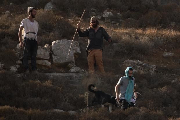 Israeli settlers walk down a hill as Israeli soldiers block...