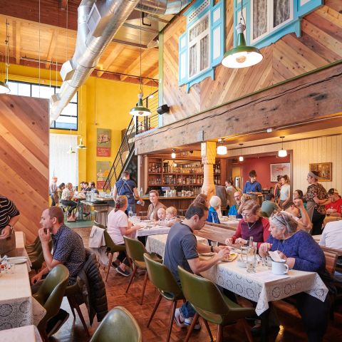 tables full of diners enjoy a meal in a lively, warmly lit restaurant with a bar in the background
