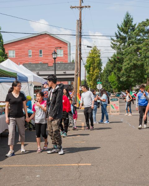 Patrons of all ages shop at a famrers market in an urban parking lot