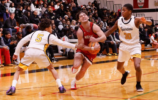 Marist's Adoni Vassilakis (center) drives through Marian's Tylor Barnes (left) and Derek Brown Jr. (right) on his way to the basket during an East Suburban Catholic Conference basketball game in Chicago Heights on Friday, Dec. 19, 2025. (John Smierciak/Daily Southtown)