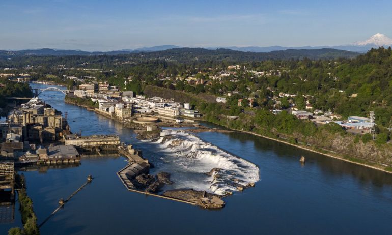 aerial view of deep blue river water at falls on the edge of a verdant cityscape