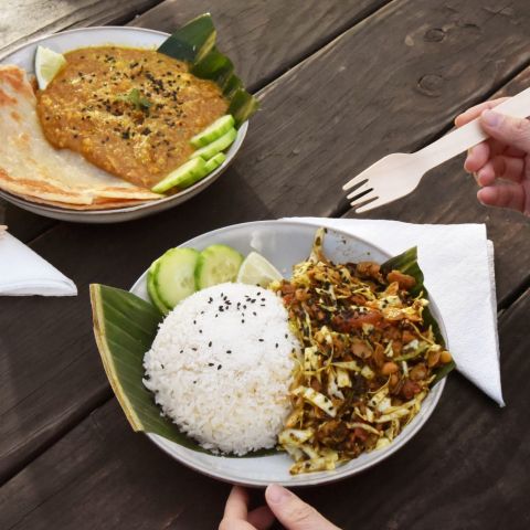 a dish of Burmese curry with flatbread and a dish of cabbage salad with rice atop a wooden table