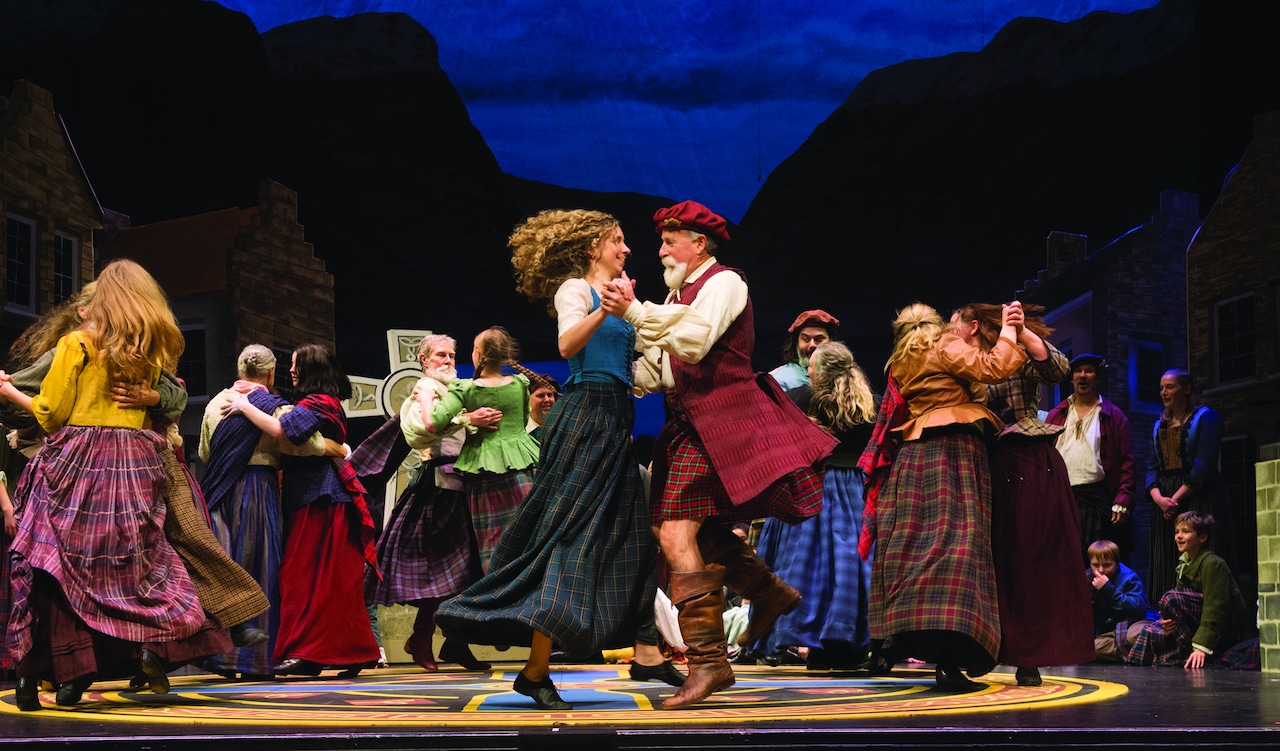 People dressed in period clothing dance on stage