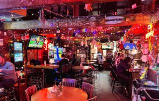 patrons sit at the bar while others play slot machines beneath exposed rafters in a warmly lit bar