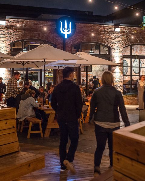 a crowd of people eat, drink and converse on an expansive, warmly lit patio at night