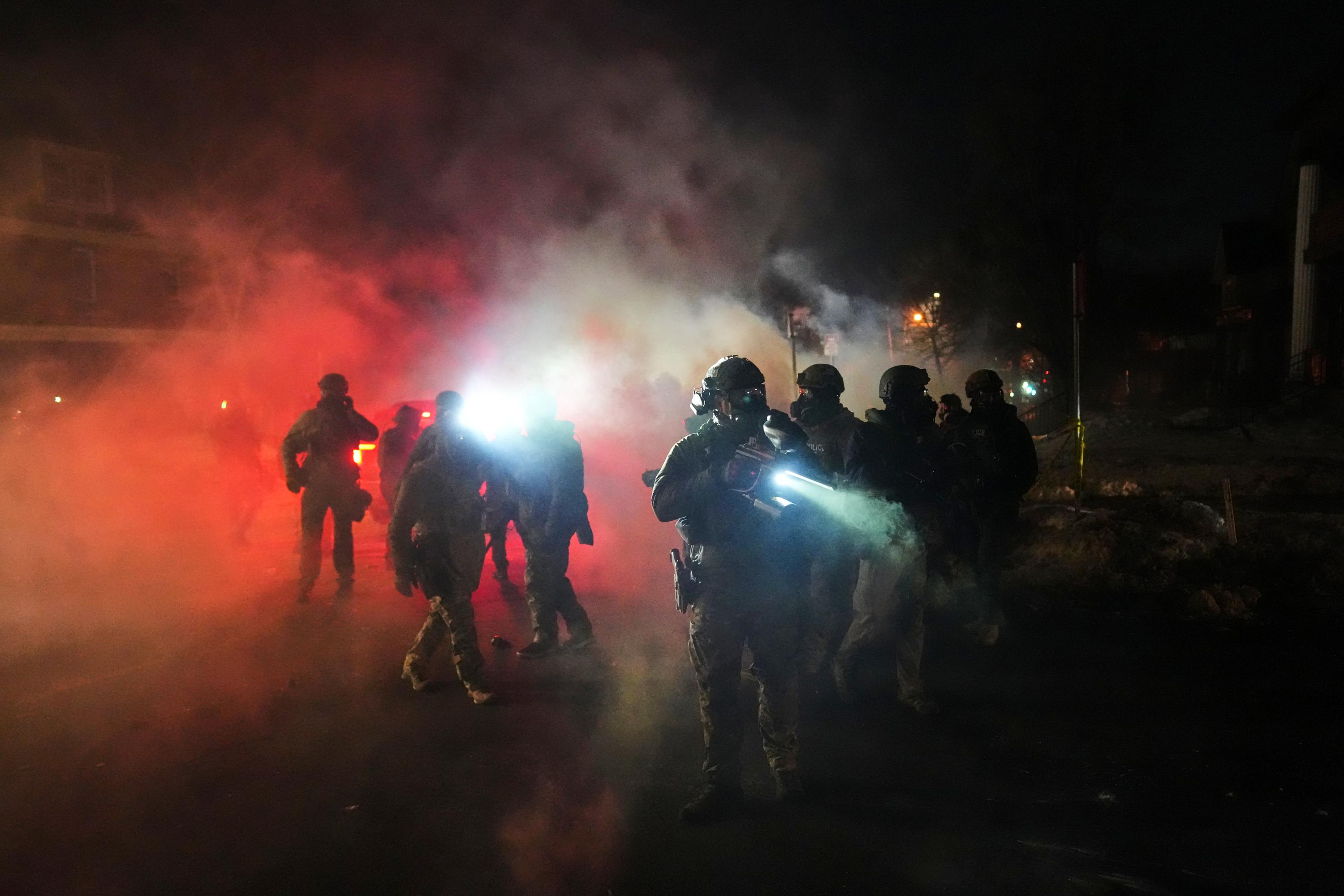 Law enforcement officers stand amid tear gas at the scene...