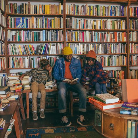 Three people sit and read a book at Mother Foucault's bookstore in front of a wall of books.