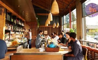 two bartenders make drinks while customers sit at the bar looking at menus