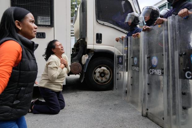 Relatives of people they consider to be detained for political reasons kneel in front of police guarding the Zona 7 Bolivarian National Police detention center in Caracas