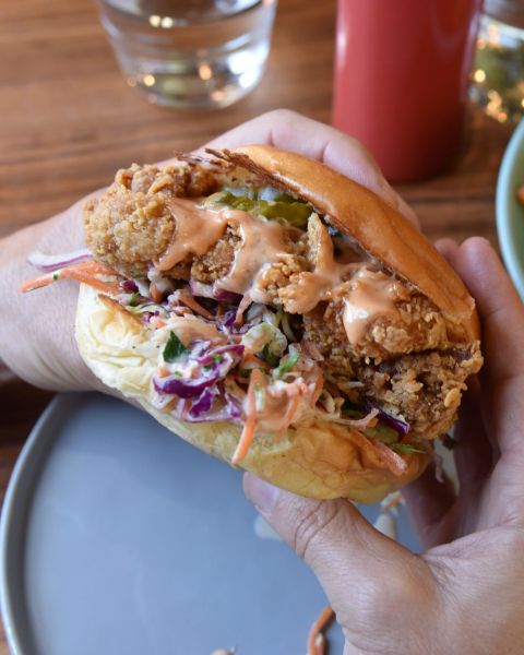 two hands hold up a delectable fried chicken sandwich complete with sauce and veggies