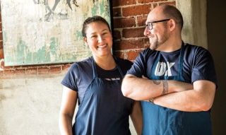 Two people stand in front of an interior brick wall smiling.