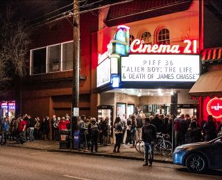 A crowd of move goers gather beneath the Cinema 21 marquee at night