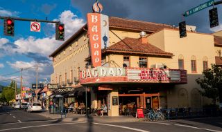 street view of an old movie house in a busy shopping district, people sit out under the marquee in a sunny spring day