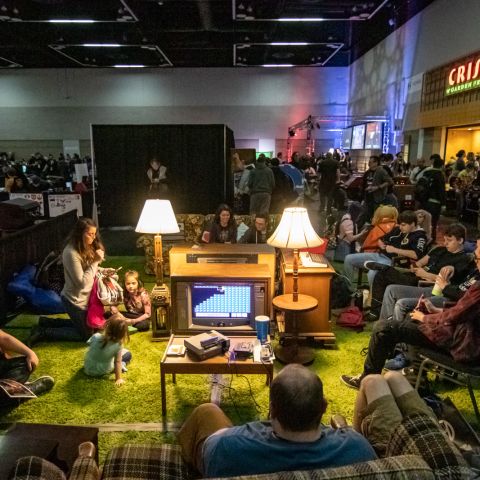gamers and onlookers gather around a vintage television set in a living room setup at a retro gaming conference