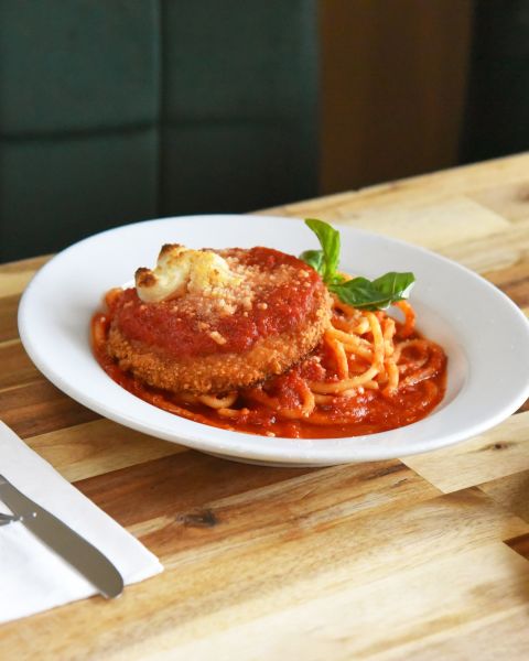 vegan chicken parmesan sits next to a pizza on a wood table