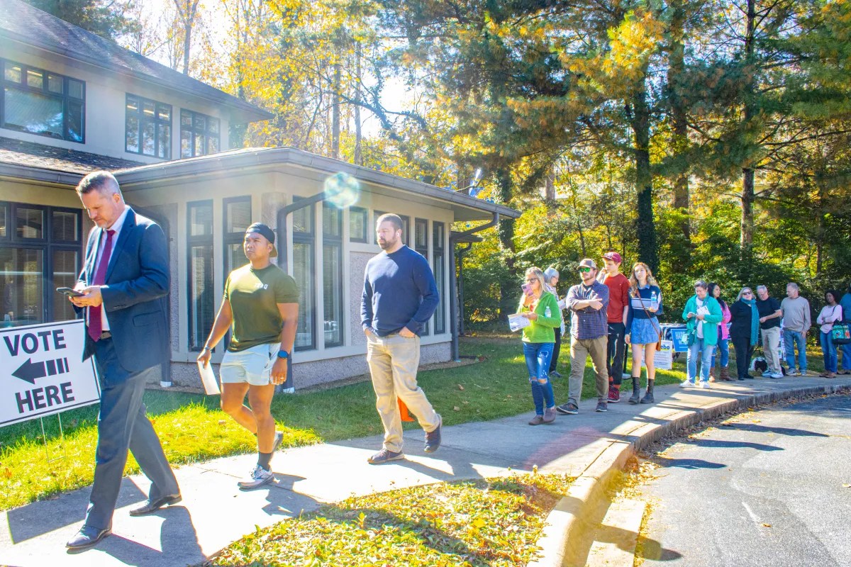 A sign says "vote here" and people wait in line