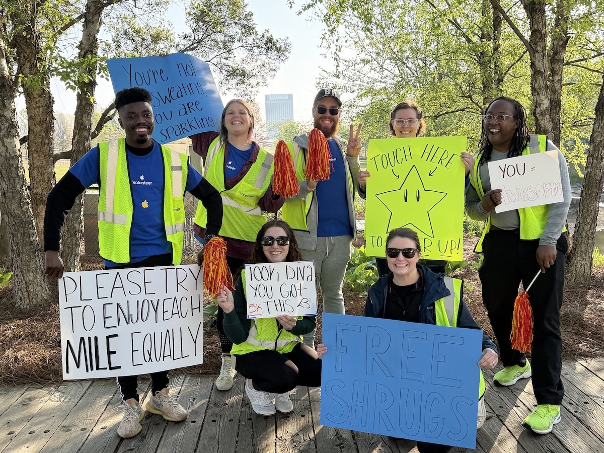 A group of volunteers hold signs cheering runners in the 2025 Red Shoe Run: Rockin' 5K in downtown Birmingham, Alabama