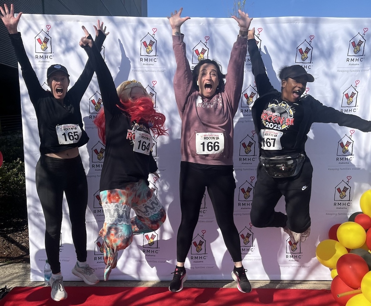 A group of runners jump for joy after completing the 2025 Red Shoe Run: Rockin' 5K in downtown Birmingham, Alabama