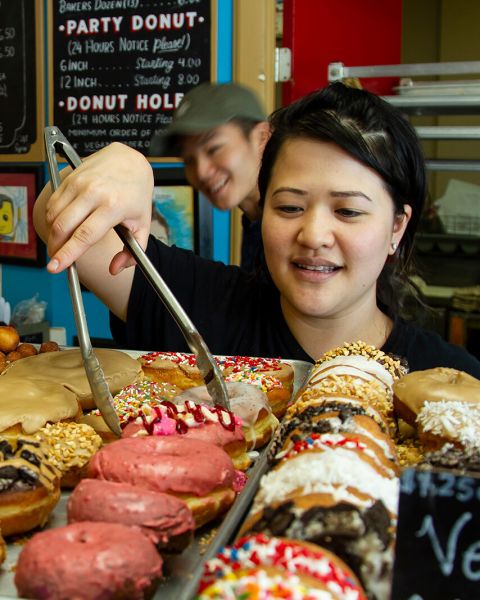 person using tongs to select a doughnut from a tray