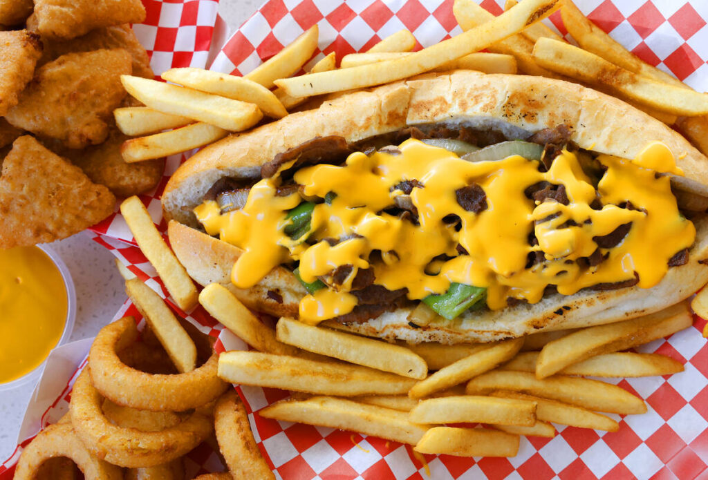 Phily cheesesteak and a side order of mac n cheese bites, onion rings and fries are displayed a ...