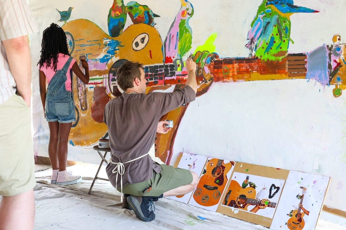 A man and young girl paint a mural of a large guitar and colorful birds at the Birmingham Folk Festival at Avondale Park in Birmingham, Alabama