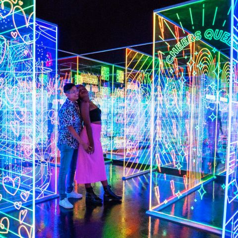 People move through a darkened space between large, clear panels illuminated with attractive glowing patterns.