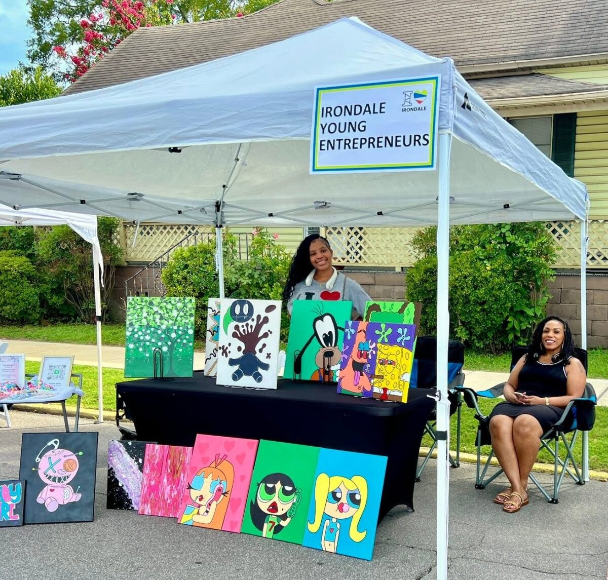 FREE I Love Irondale Day 2026 brings food, fun + tech 3 A young vendor smiles behind a table displaying colorful cartoon-themed paintings at the Irondale Young Entrepreneurs market booth