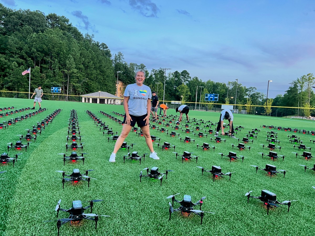 FREE I Love Irondale Day 2026 brings food, fun + tech 9 A smiling woman in an Irondale shirt stands among hundreds of drones lined up on a field, ready for launch
