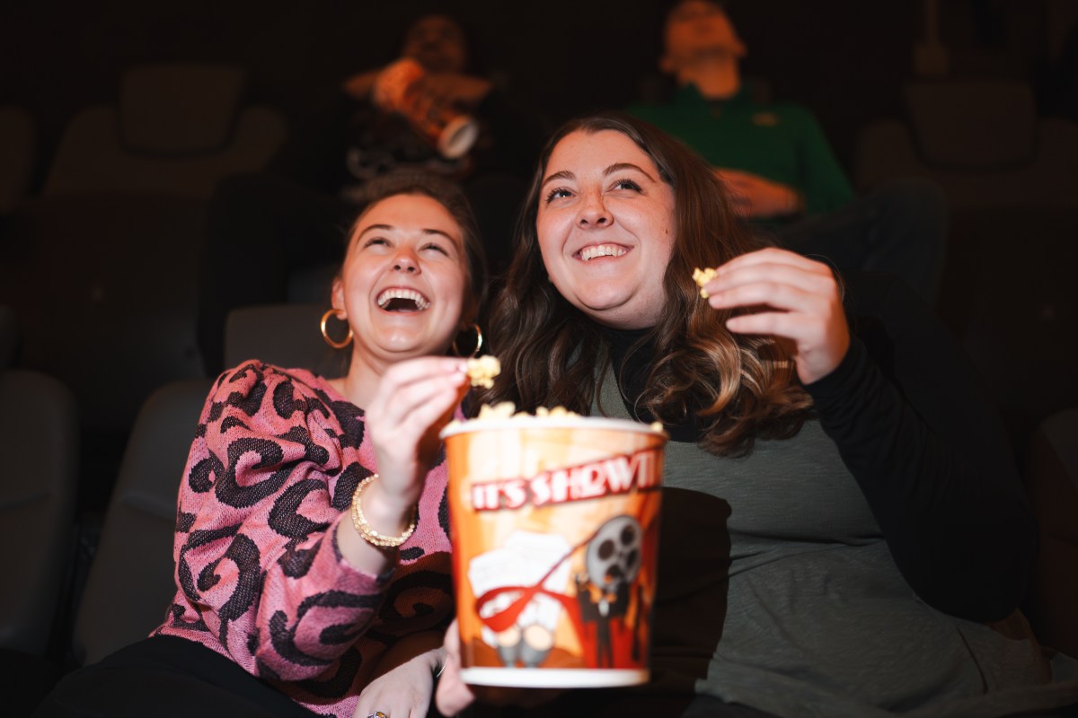 Two women laughing and sharing popcorn while watching a movie at McWane Science Center's IMAX Dome Theater