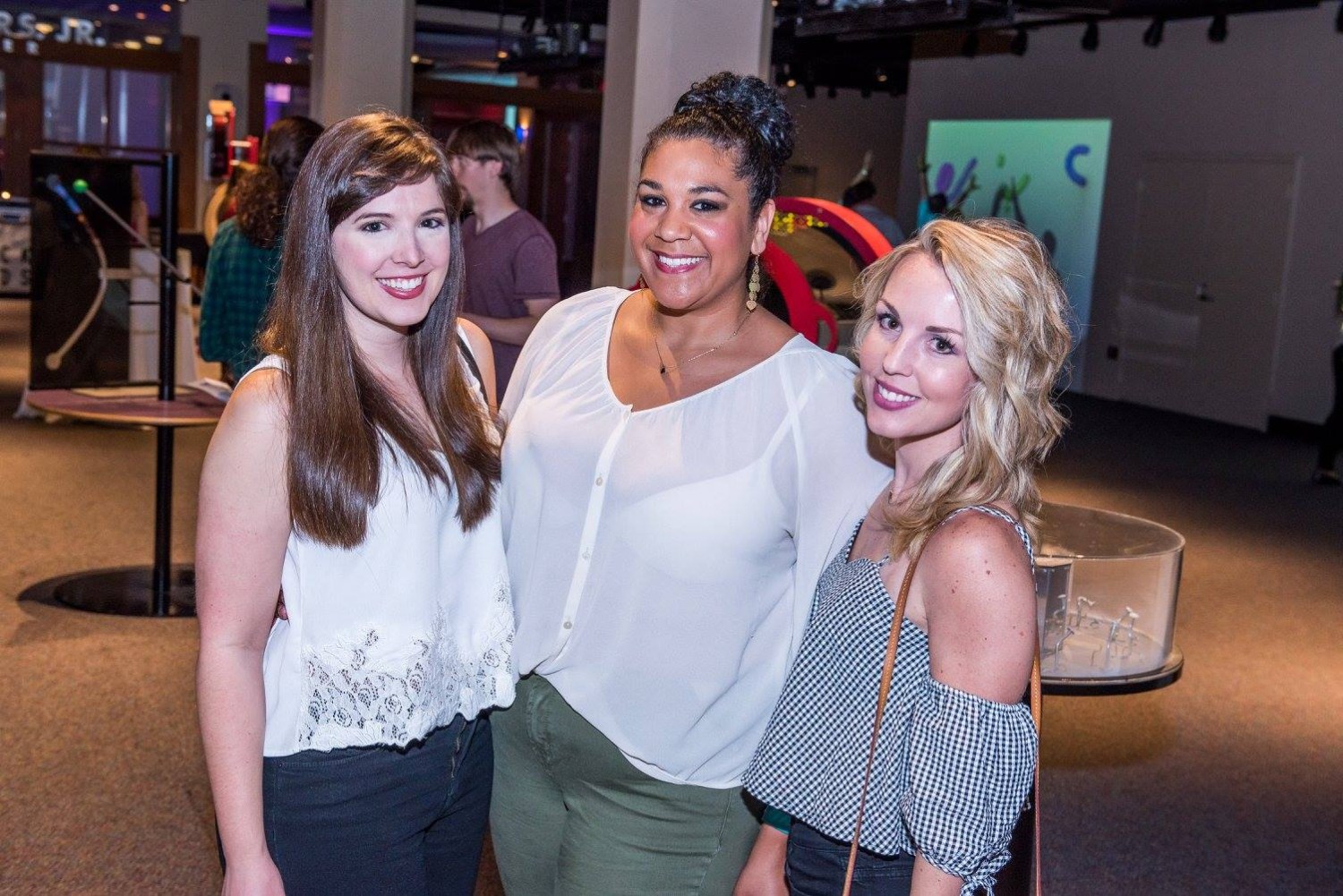 Three women smiling together during a McWane After Dark adult evening event at McWane Science Center