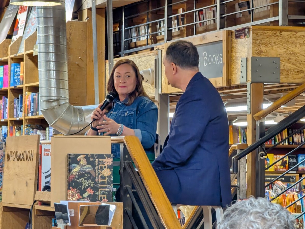 Shelby Van Pelt speaking at a bookstore event alongside Jamie Ford, surrounded by shelves of books