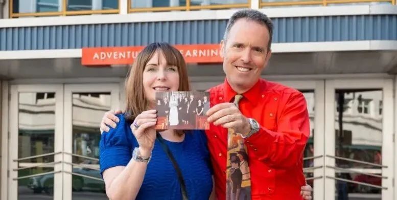 close up of woman in blue shirt and man in red shirt holding a wedding picture on a date at McWane Science Center in Birmingham