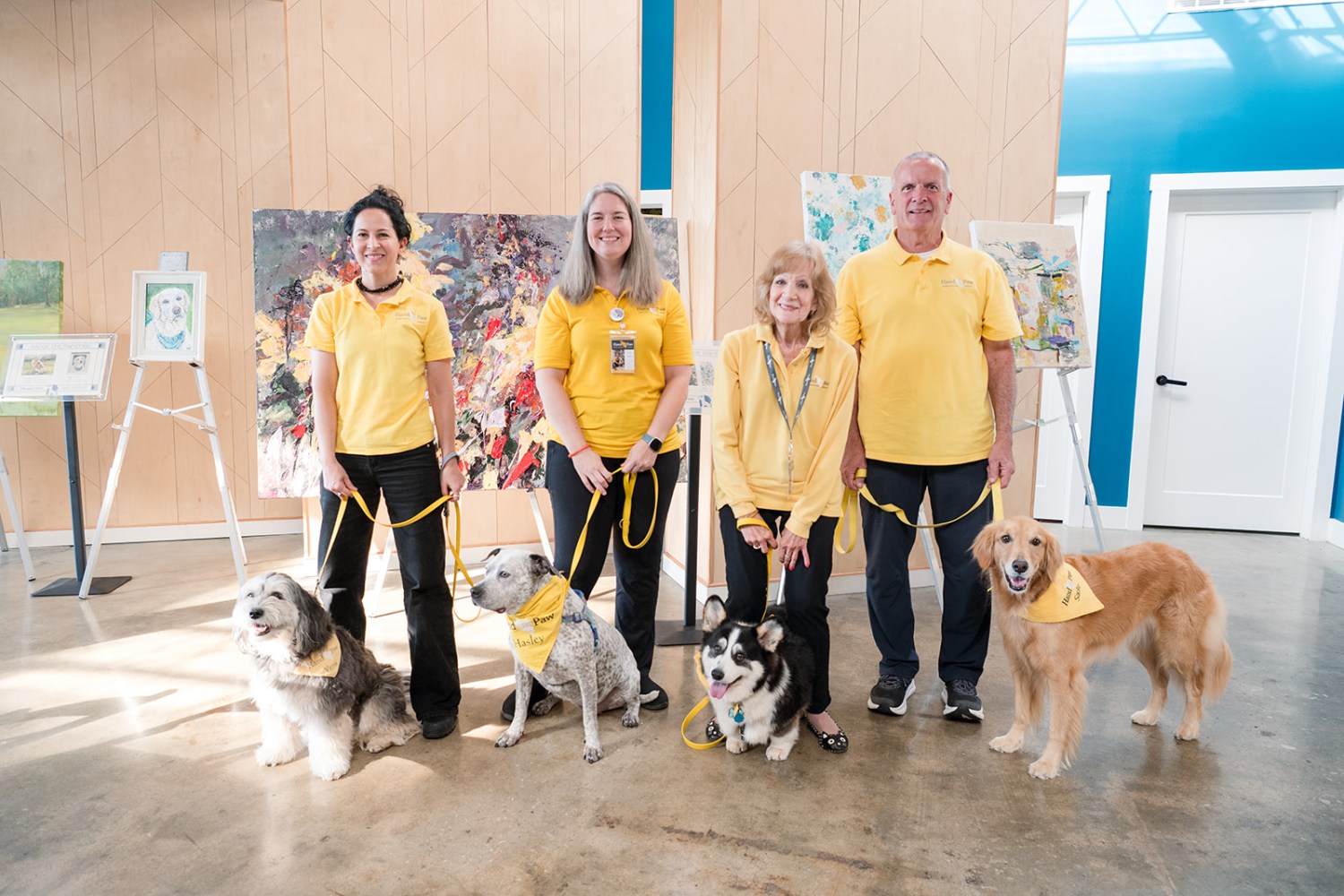 How to get tickets now for the Picasso Pets gala—give back + win a trip to Italy, August 22 7 Four therapy dog handlers in yellow shirts pose with their dogs wearing yellow bandanas in front of colorful artwork on easels