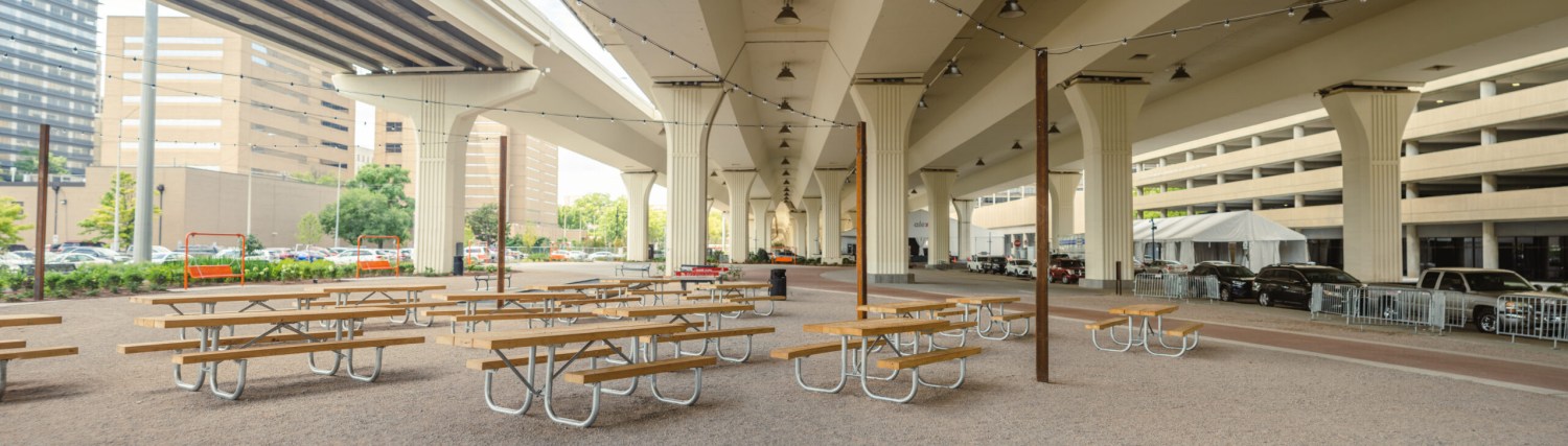 Everything you need to know about FISE in Birmingham Aug 7-9: world-class sports, live music + more 3 Outdoor seating area with wooden picnic tables under an elevated structure with string lights in an urban setting