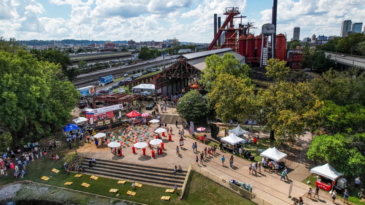 Aerial view of an outdoor festival at Sloss Furnaces in Birmingham, Alabama, with vendor tents, umbrellas, and crowds of attendees