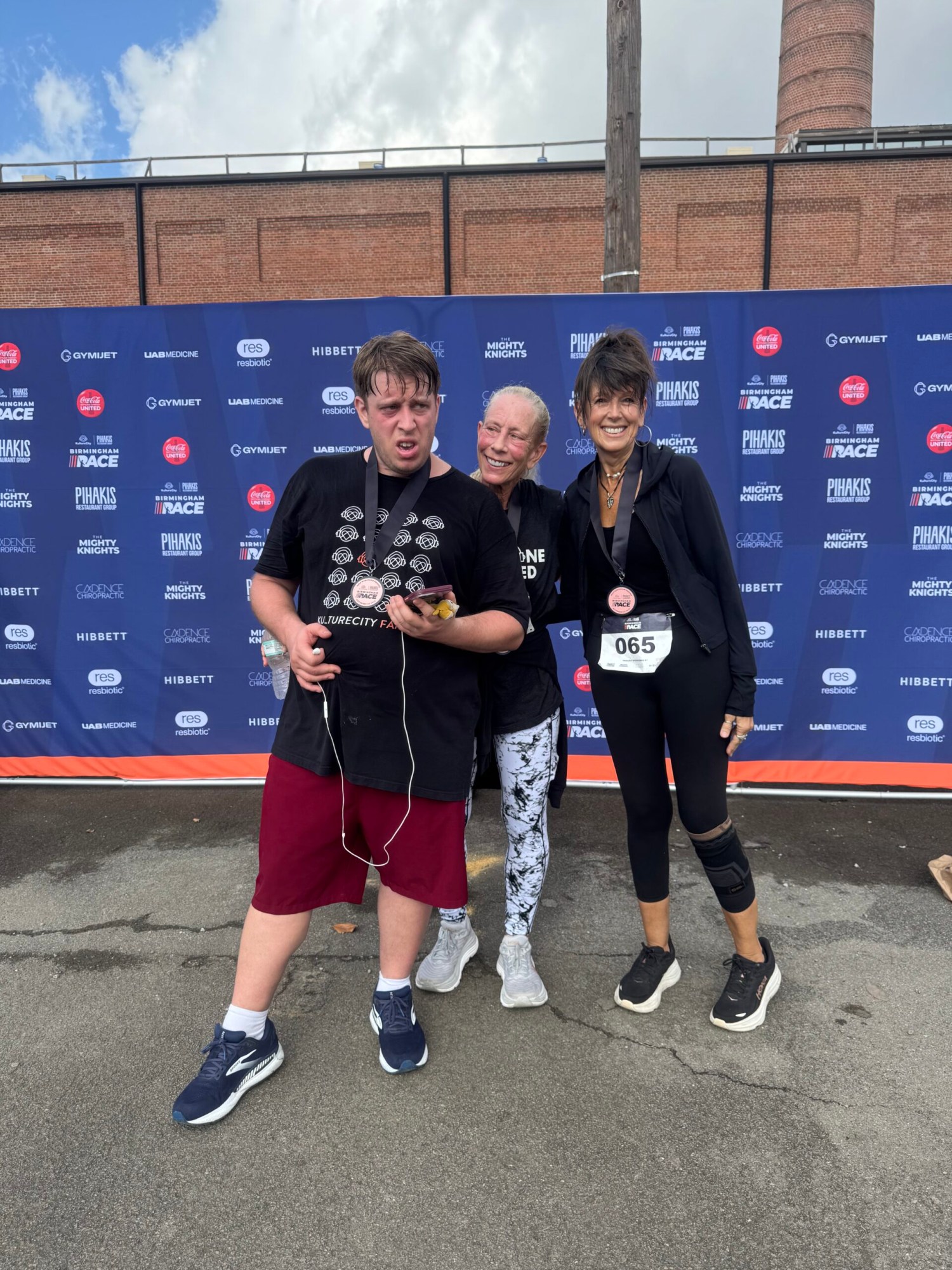 Three runners wearing finisher medals pose together in front of a Birmingham Race Series sponsor backdrop after the event