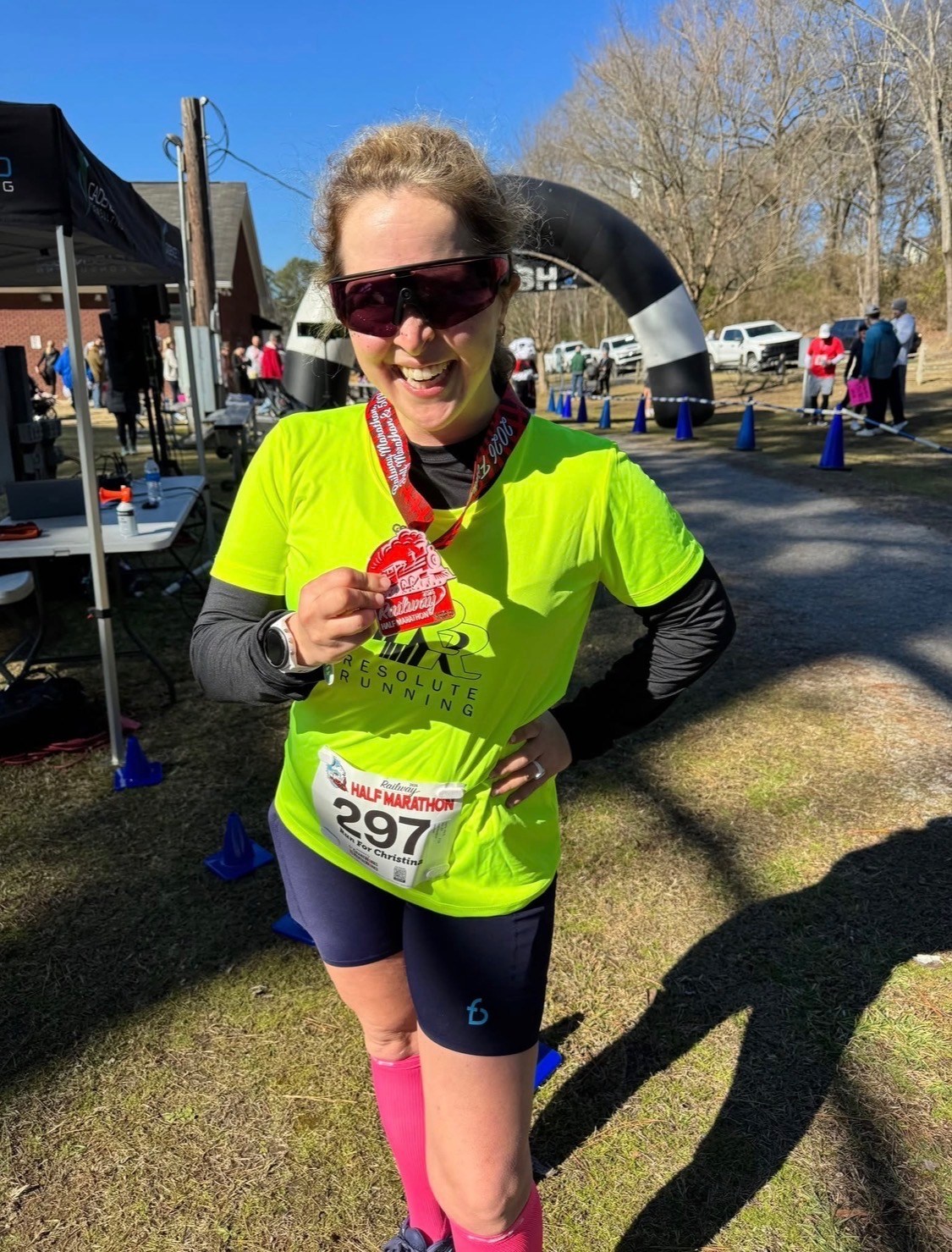 Smiling runner in neon yellow shirt and bib 297 holding a Railway Half Marathon finisher medal